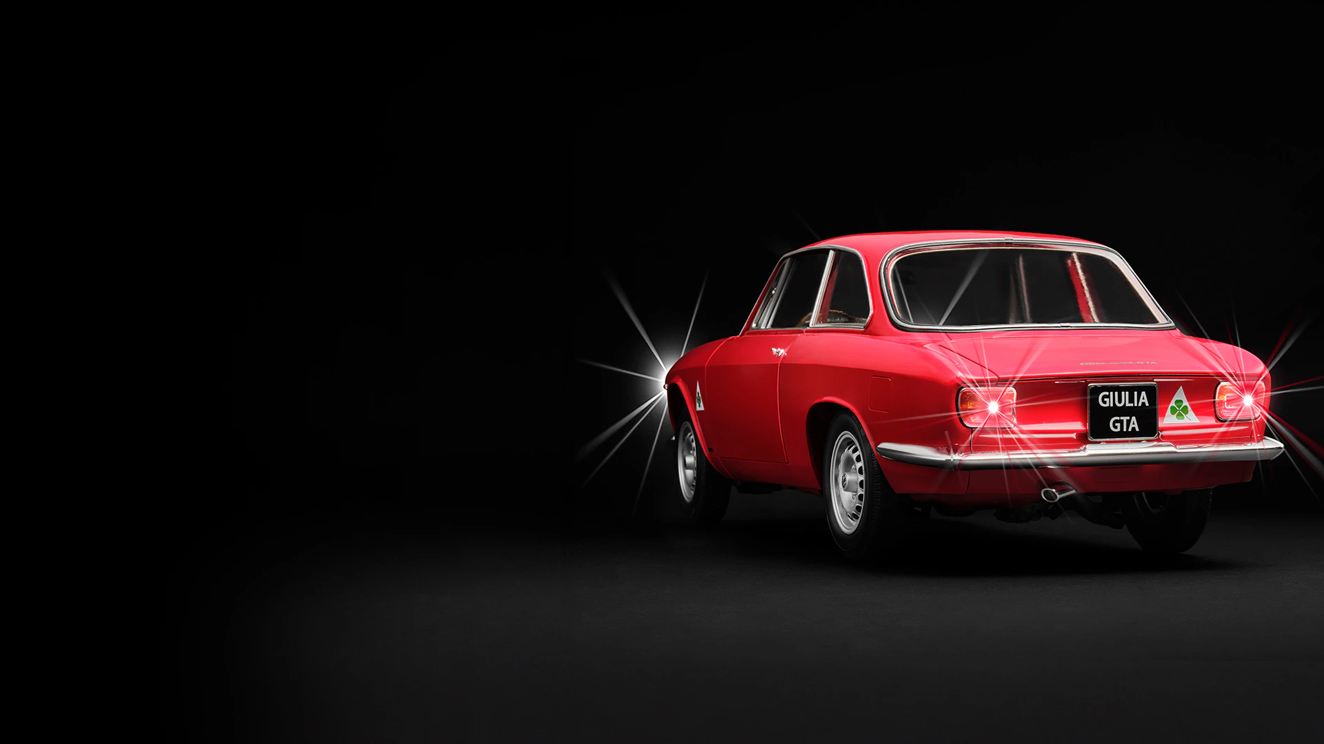 Immagine di un’auto d’epoca Alfa Giulia Sprint rossa su sfondo nero. L’immagine include il testo promozionale: “Il primo invio a solo 1€”