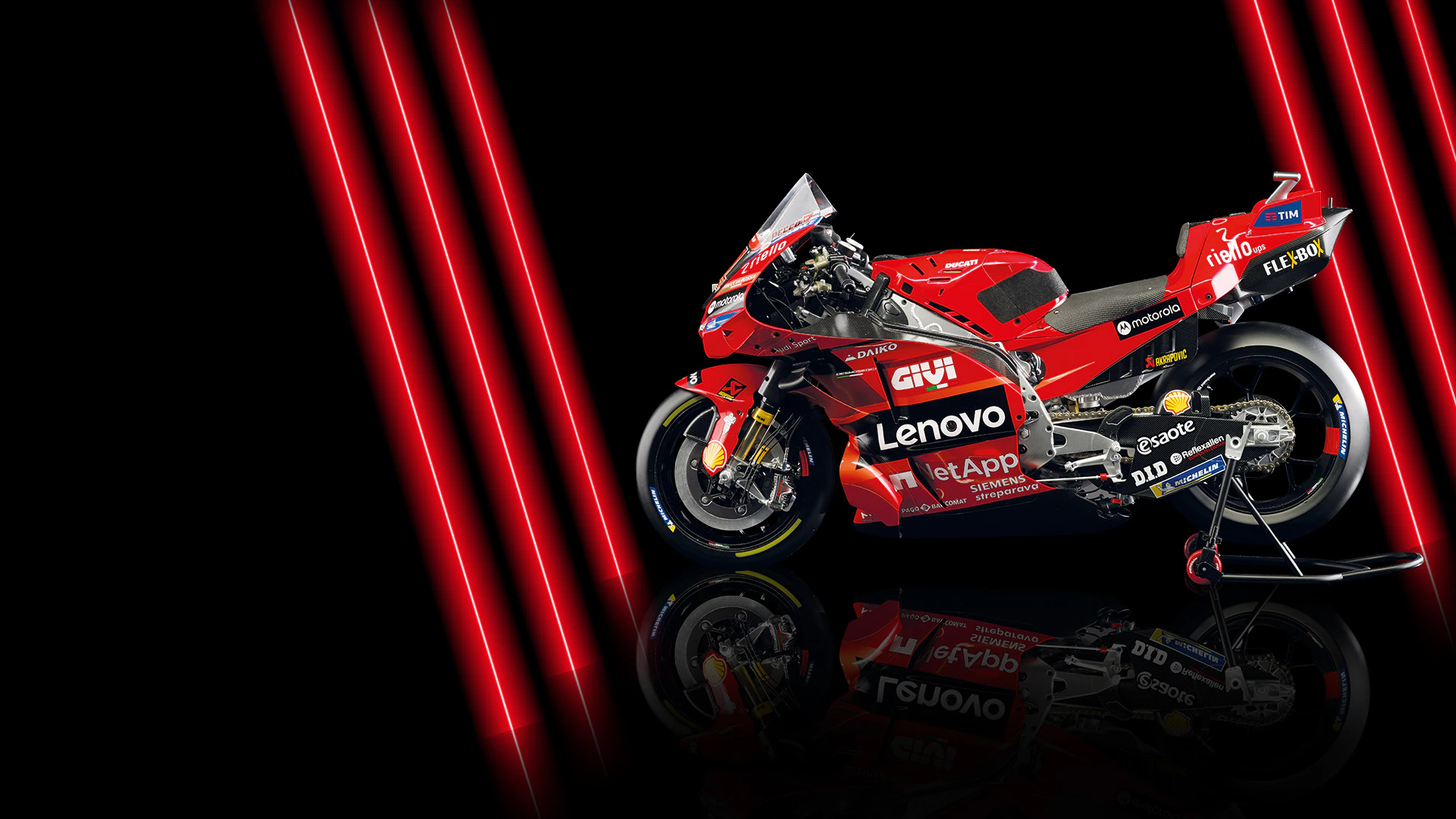 Immagine di una moto Ducati rossa su sfondo nero con luci al neon rosse. L’immagine include il testo promozionale: “Primo invio a solo 1 €”